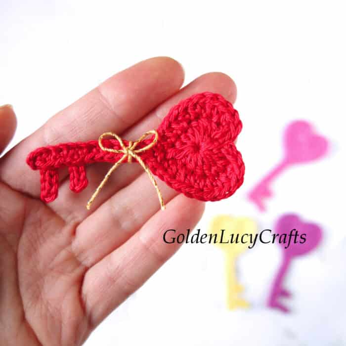 Red crochet heart-shaped key in the palm of a hand.