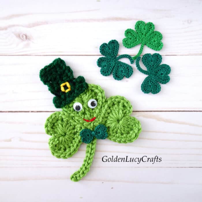 Crochet appliques large shamrock in a hat with googly eyes and three small shamrocks.
