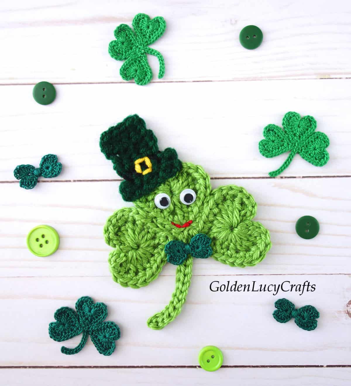 Large crocheted shamrock in a hat in a middle, small shamrocks and green buttons around.