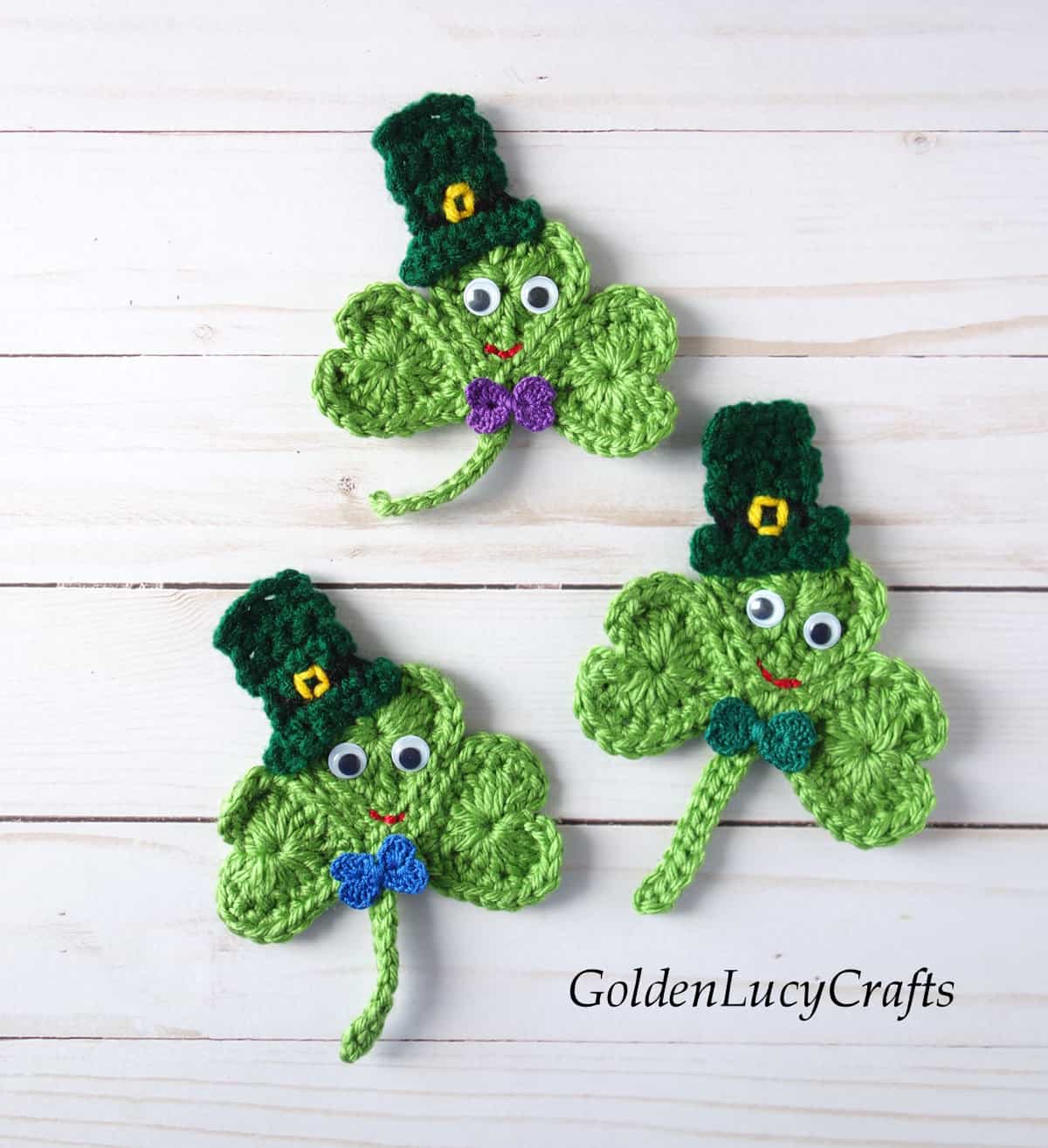 Three crocheted shamrocks in hats and with googly eyes.