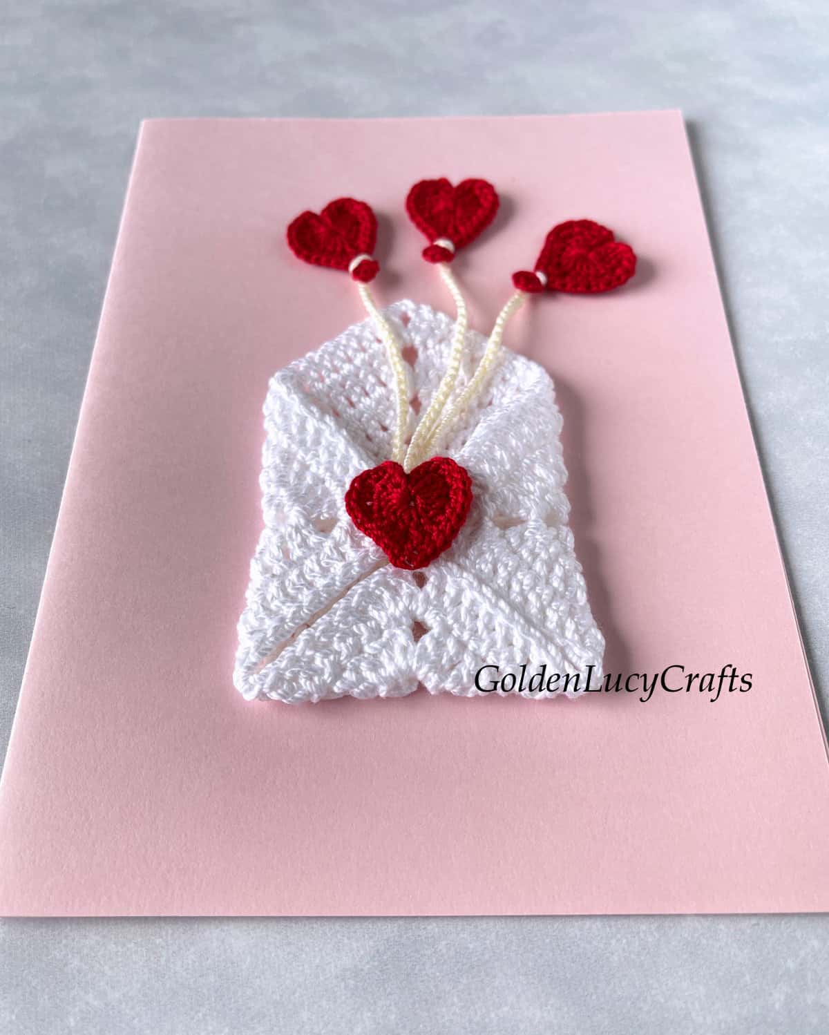 Pink card with crochet heart envelope and heart balloons.