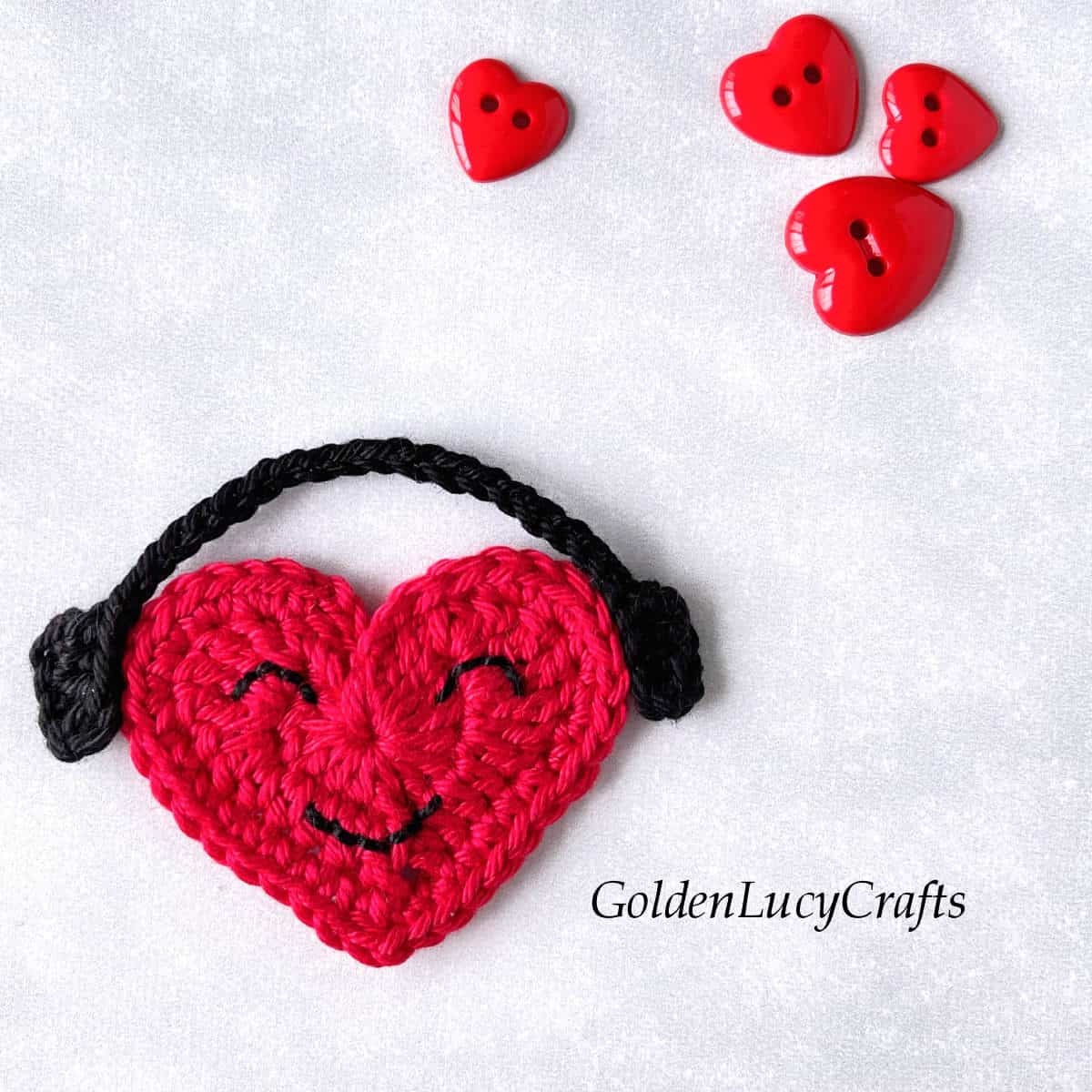Crochet red heart with smiley face and black headphones.