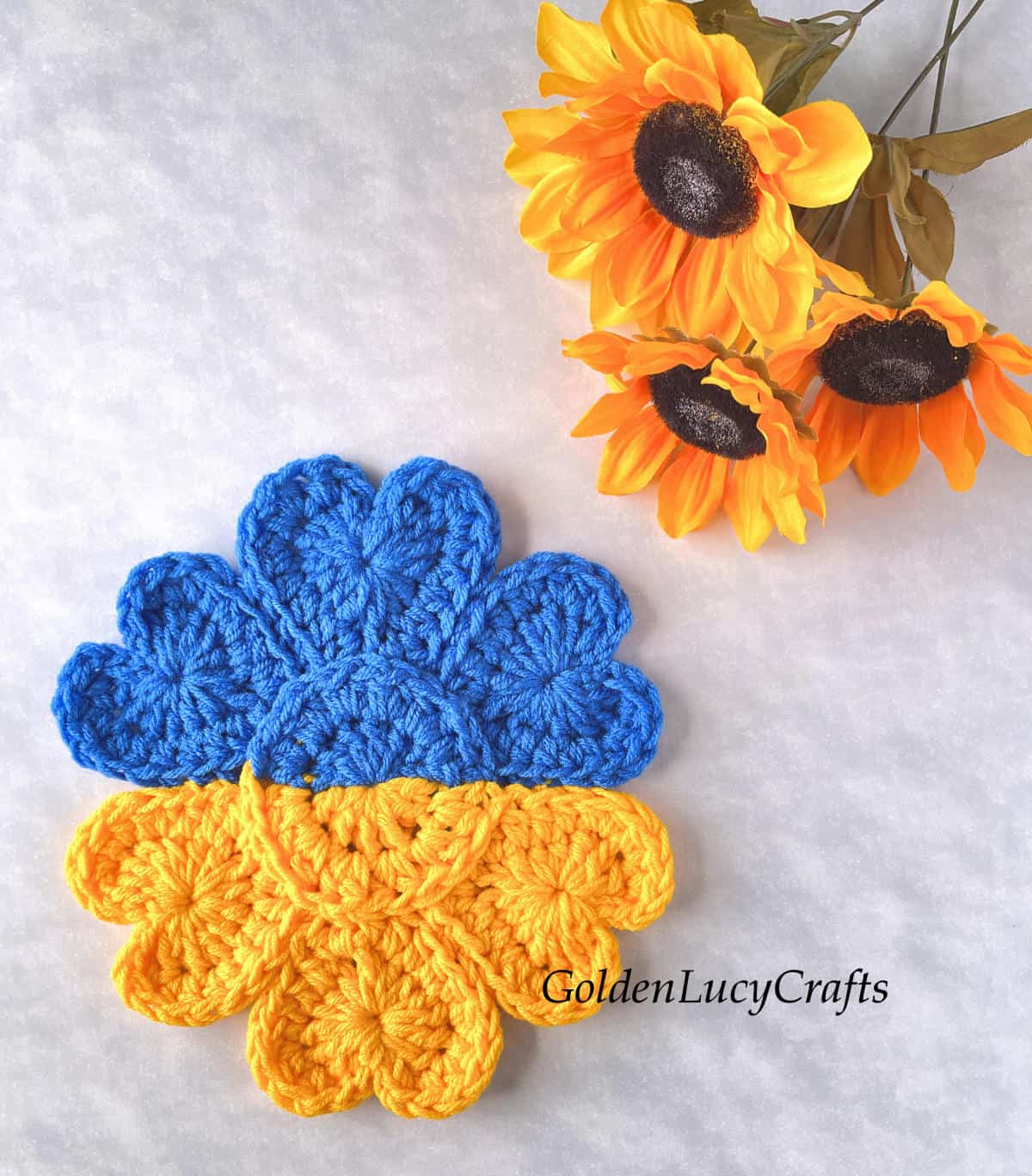 Crochet flower made in colors of Ukrainian flag, sunflowers in the background.