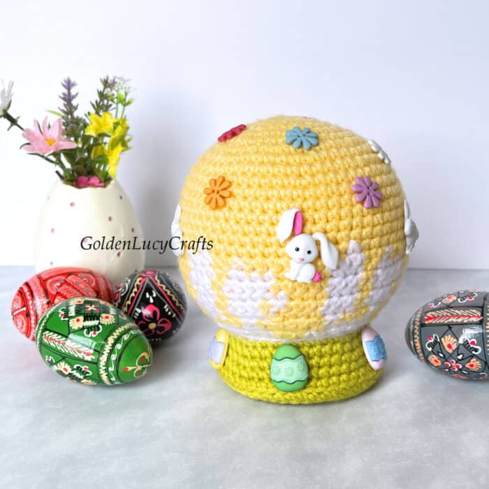 Crochet Easter snow globe, decorated Easter eggs next to it.