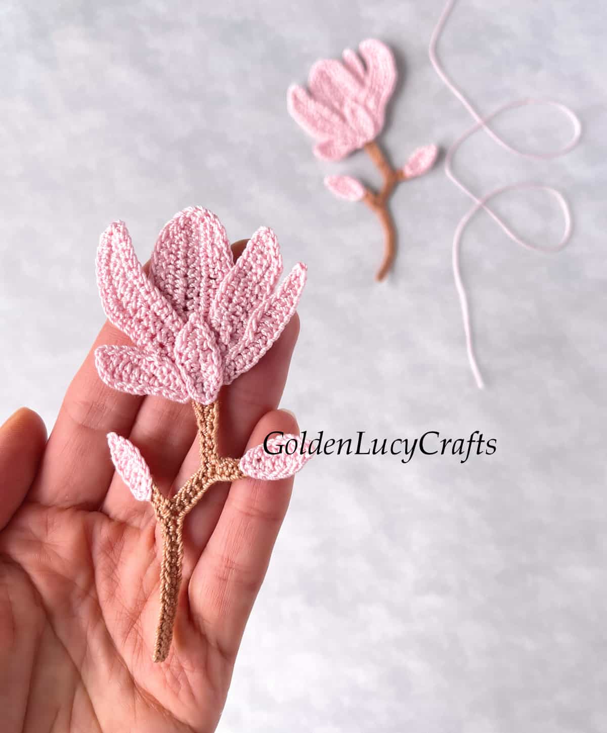 Crochet pink magnolia applique in the palm of a hand.