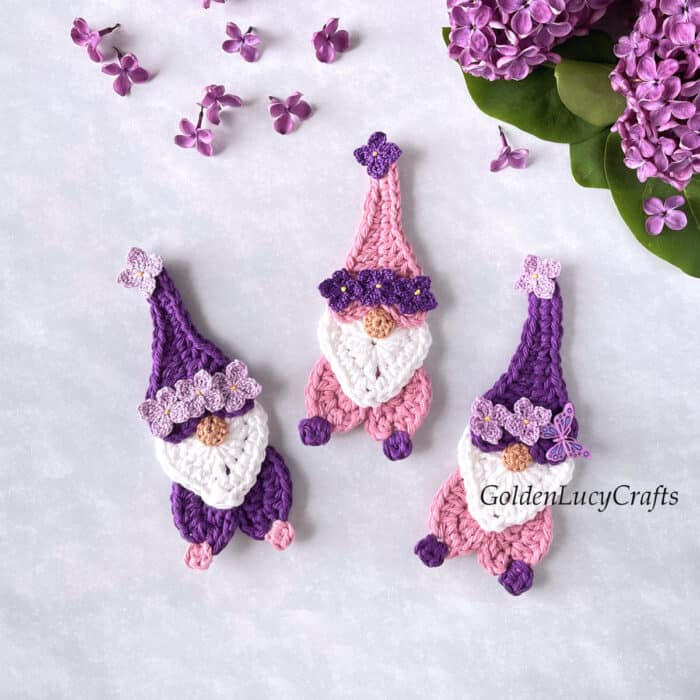 Three crochet Mother's Day gnomes, lilac flowers in the background.