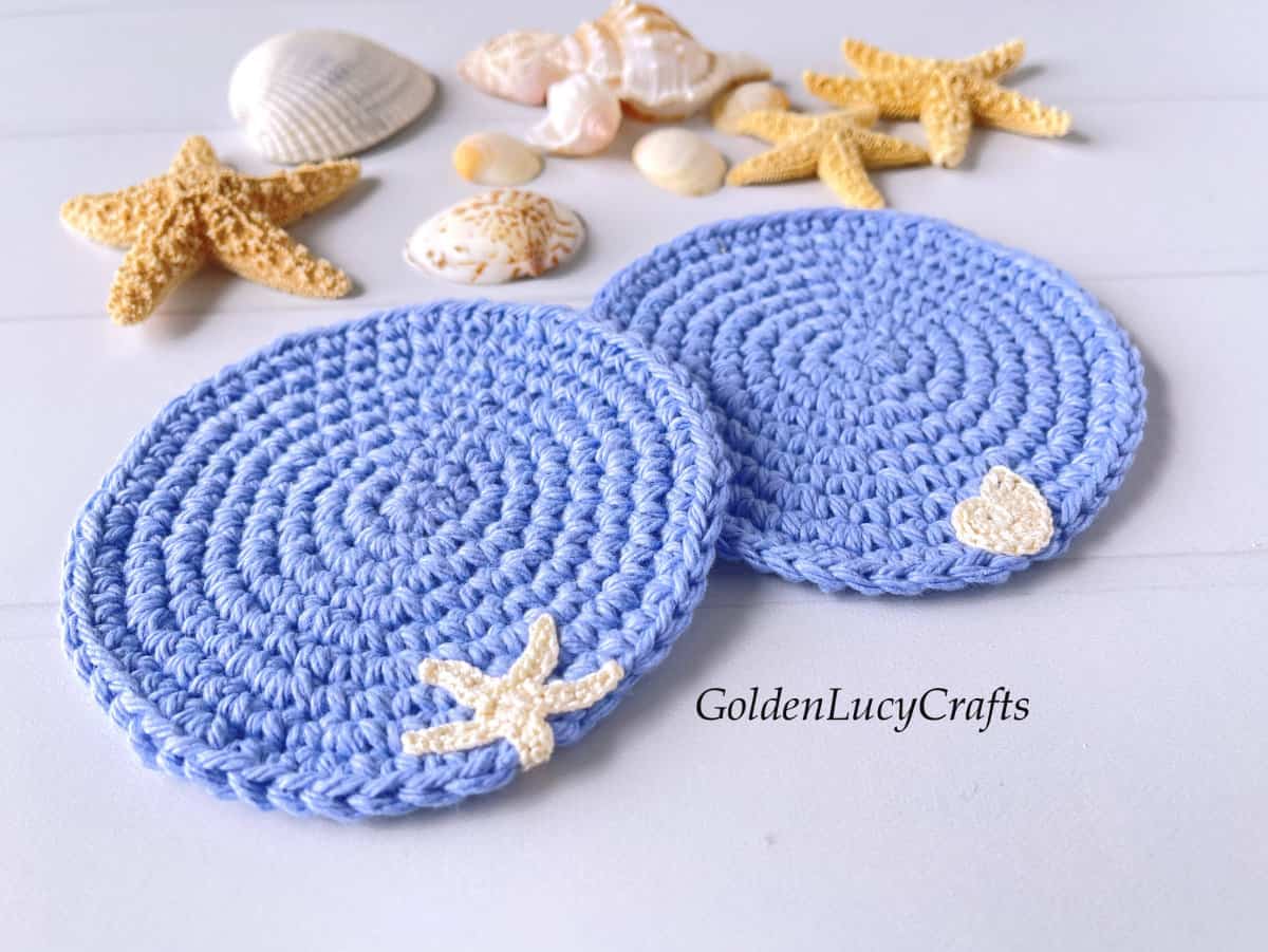 Crocheted ocean themed blue coasters, sea stars and sea shells in the background.
