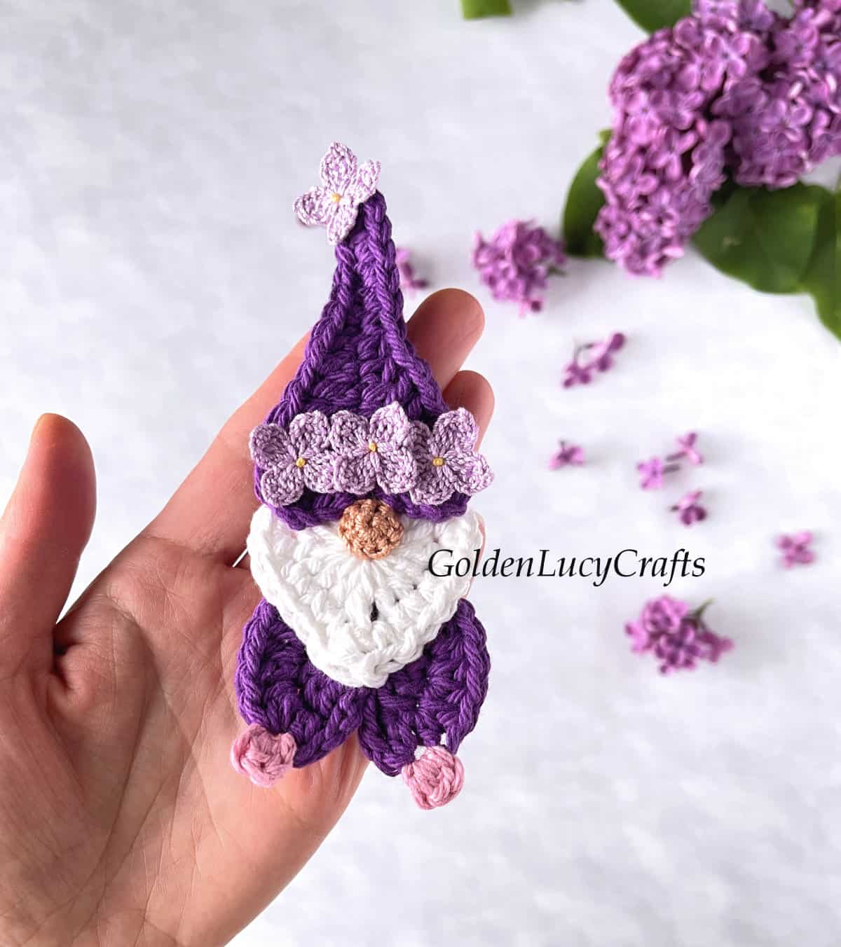 Crochet lilac gnome in the palm of a hand.