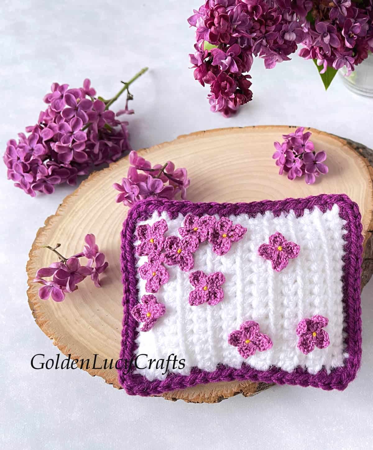 Crochet mini pillow or pincushion embellished with crocheted lilac flowers.