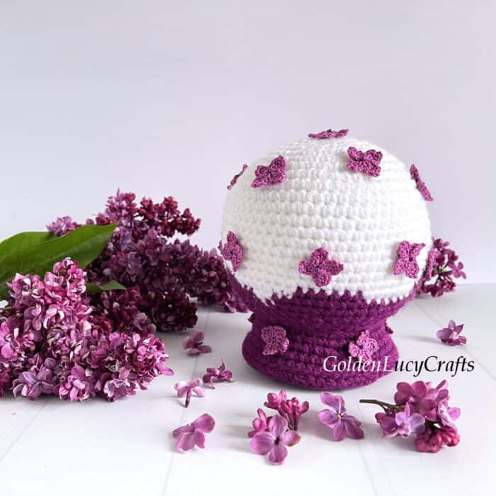 Crochet lilac snow globe, lilac flowers laying next to it.