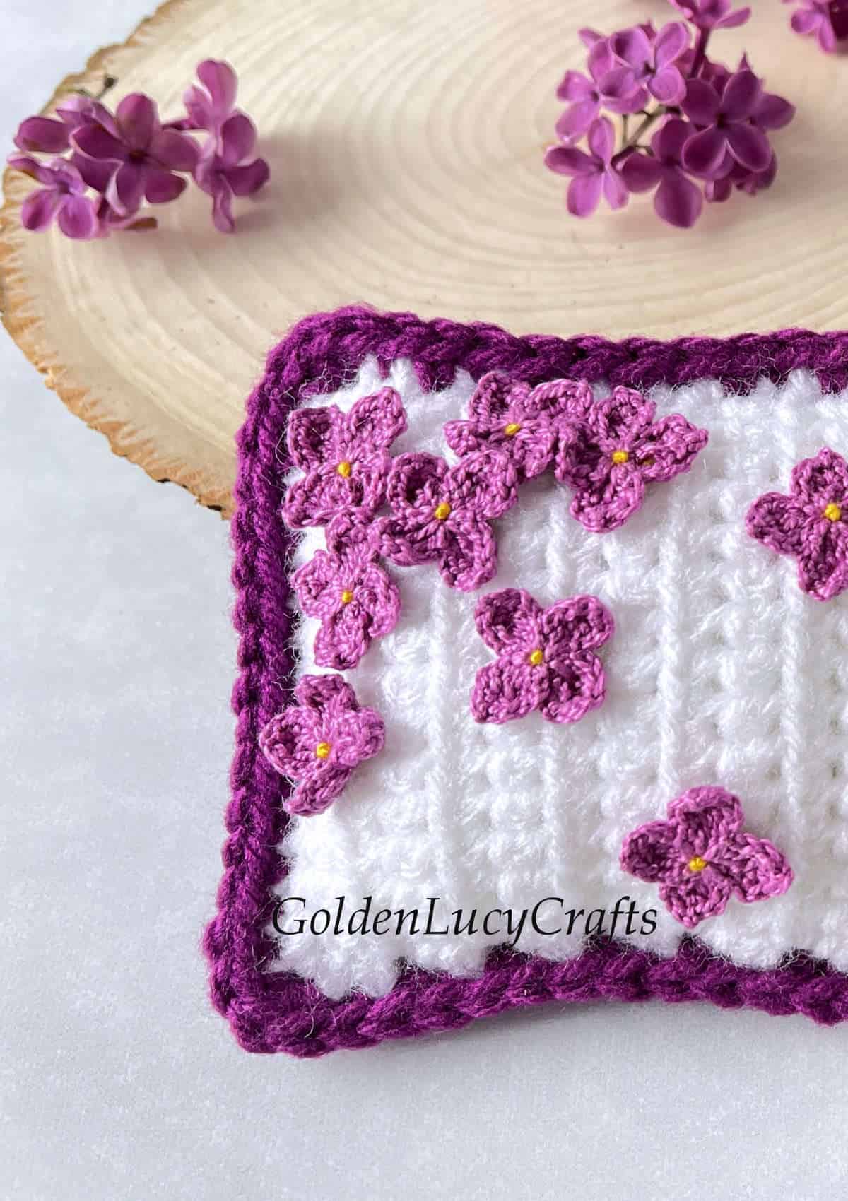 Crochet decorative mini pillow embellished with crocheted lilac flowers close up picture.