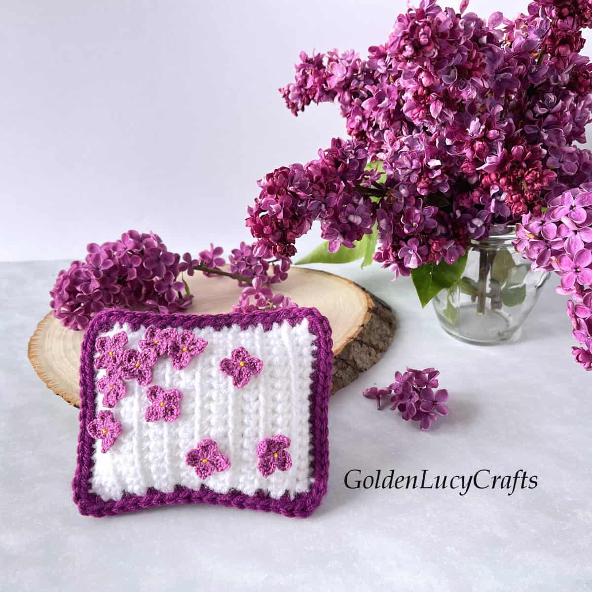 Crochet decorative mini pillow embellished with crocheted lilac flowers.