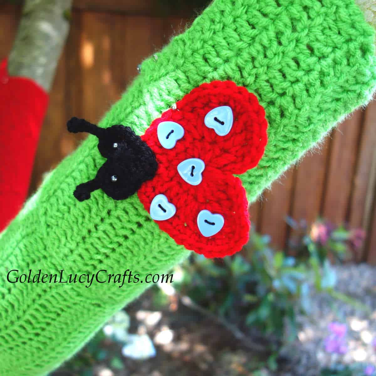 Tree branch wrapped in green crocheted fabric embellished with ladybud applique.