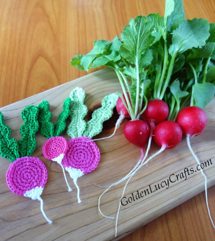 Crocheted and real radishes on the wooden board.
