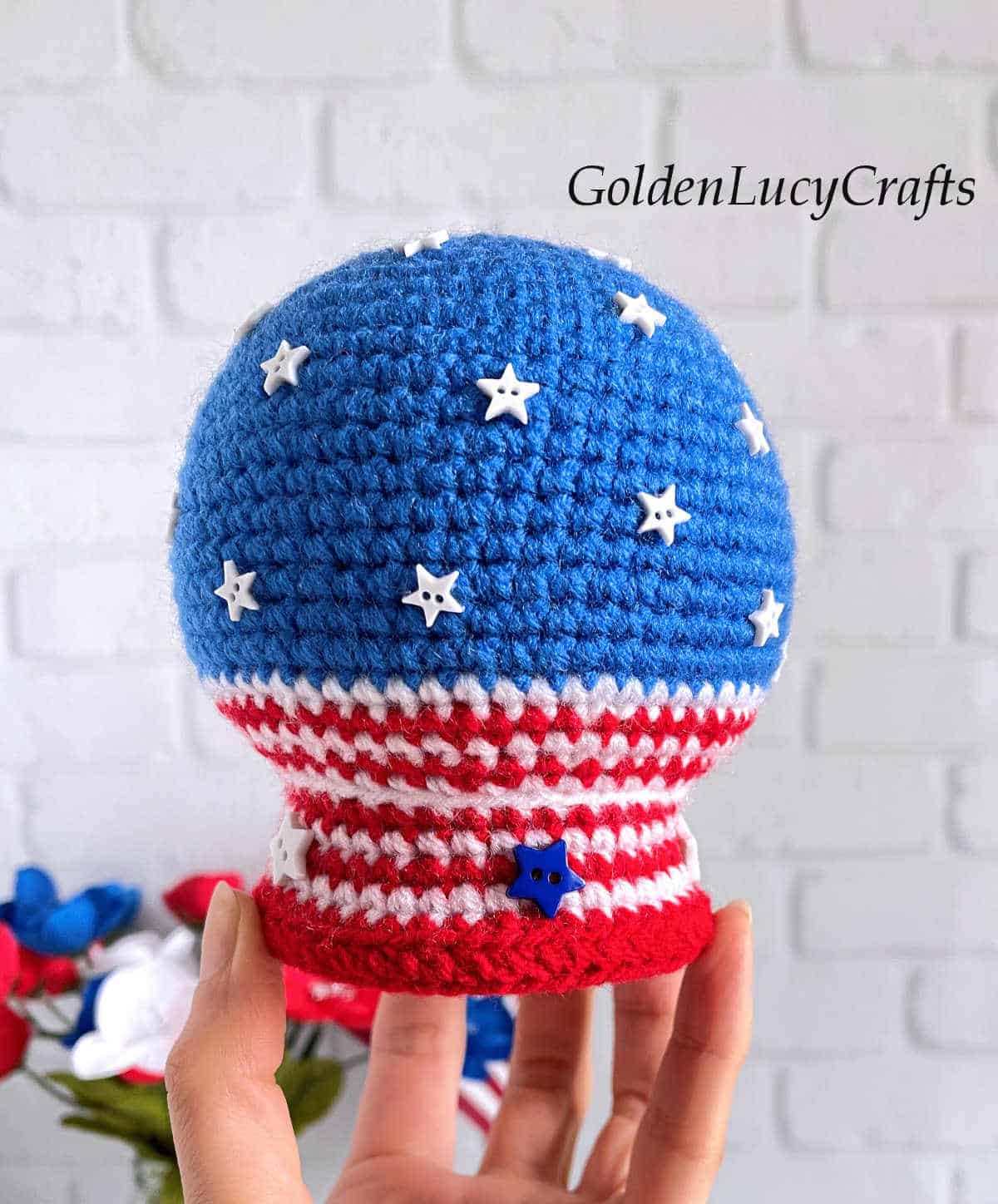 Crochet patriotic snow globe held by finger tips.