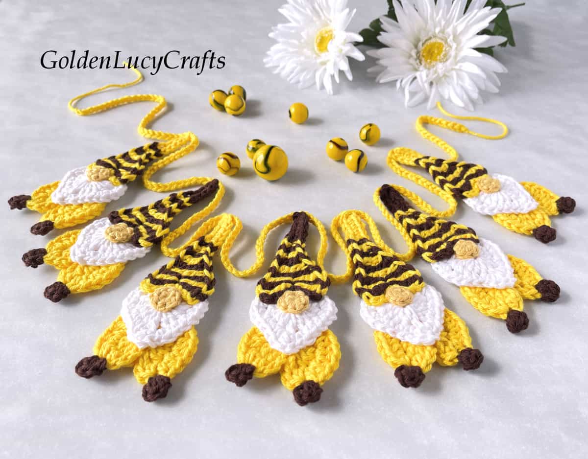 Crocheted bee gnome garland, daisies in the background.