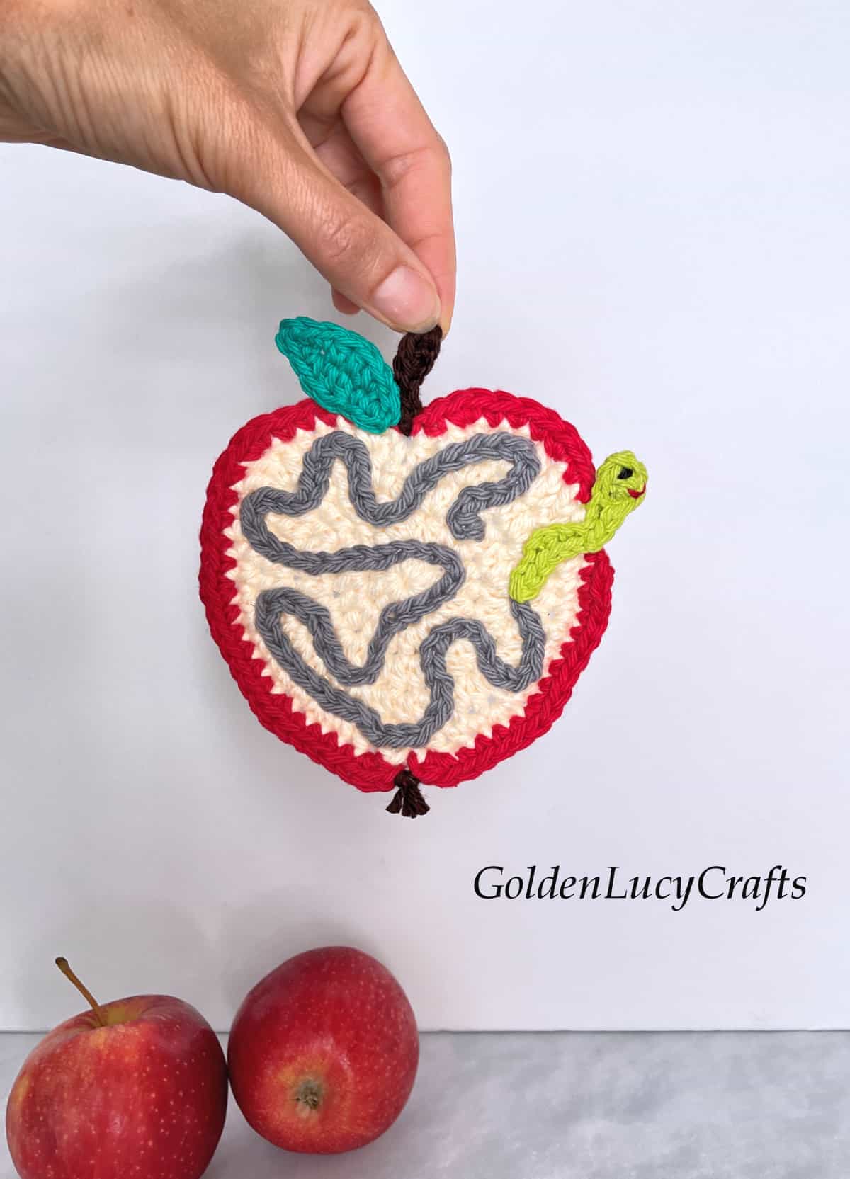 Crochet apple with worm coaster held by fingertips.