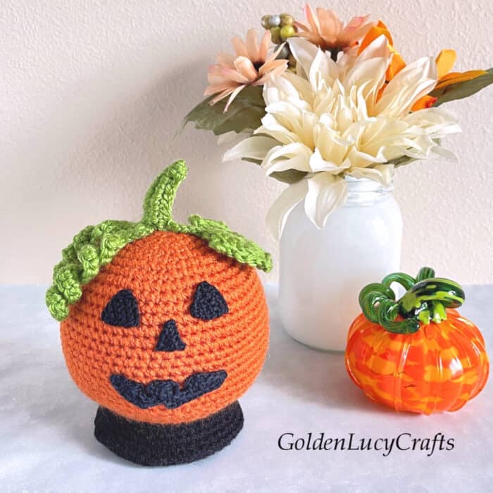 Crocheted Halloween pumpkin snow globe, white vase with flowers and small glass pumpkin.