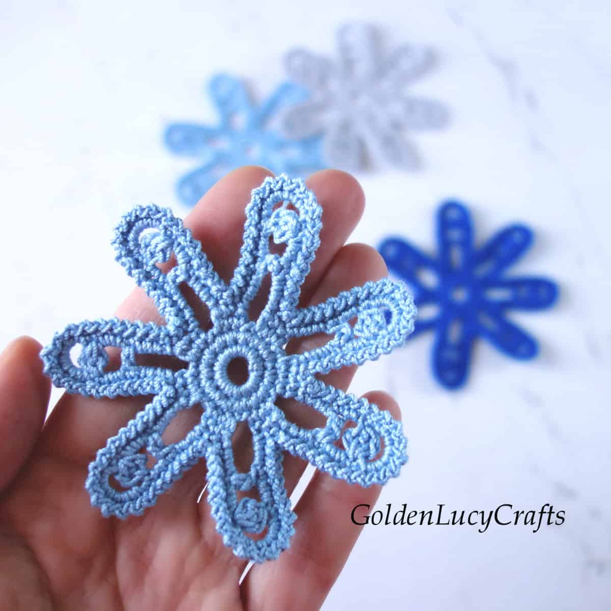 Crochet light blue flower in the palm of a hand.