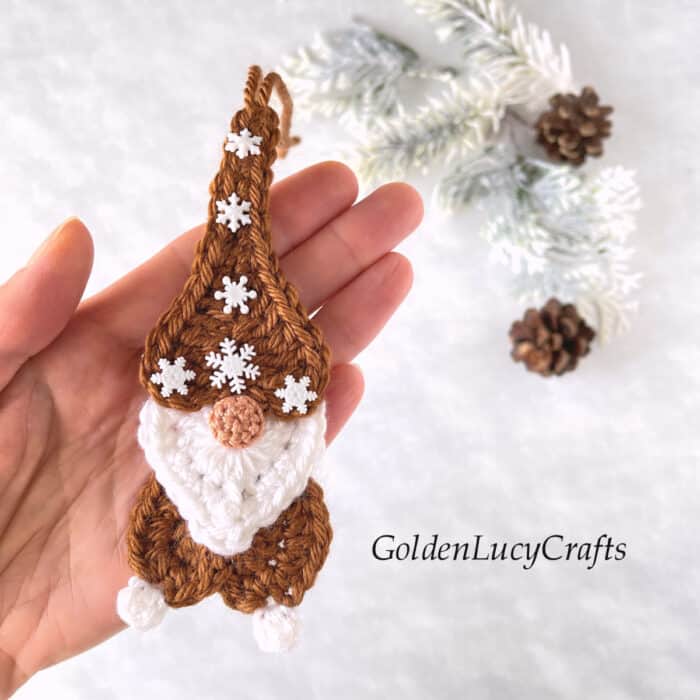Crochet gingerbread gnome in the palm of a hand.