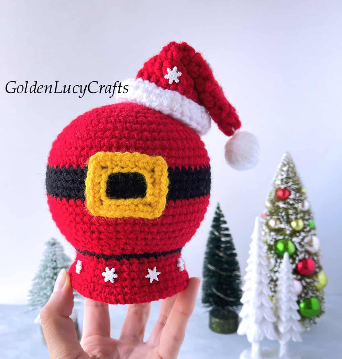 Crochet Santa belly snow globe held by finger tips.