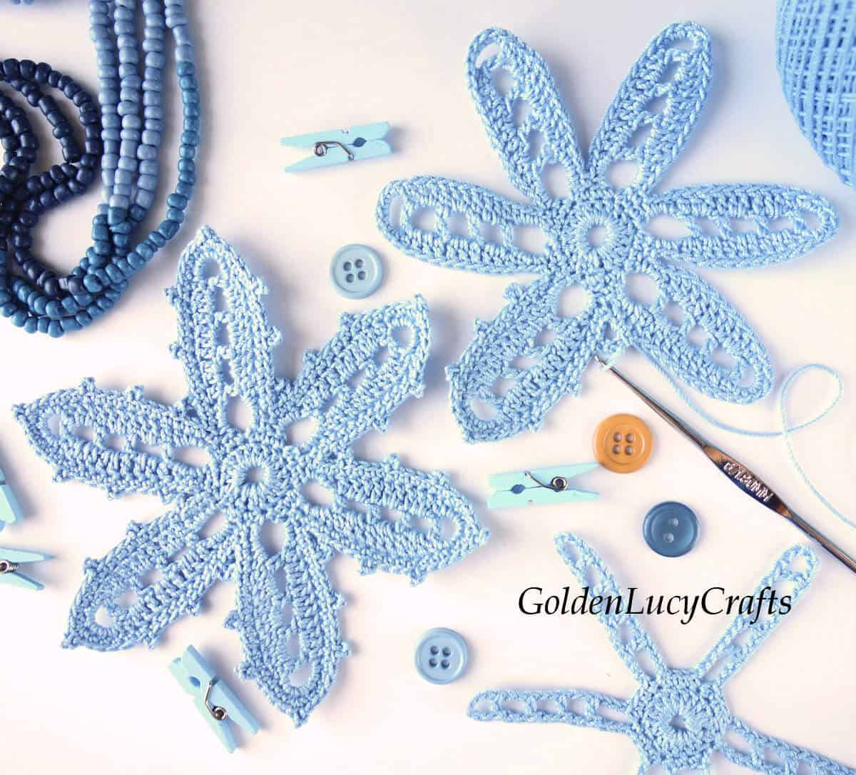 Crocheted light blue flowers, buttons, crochet hook and clothespin.