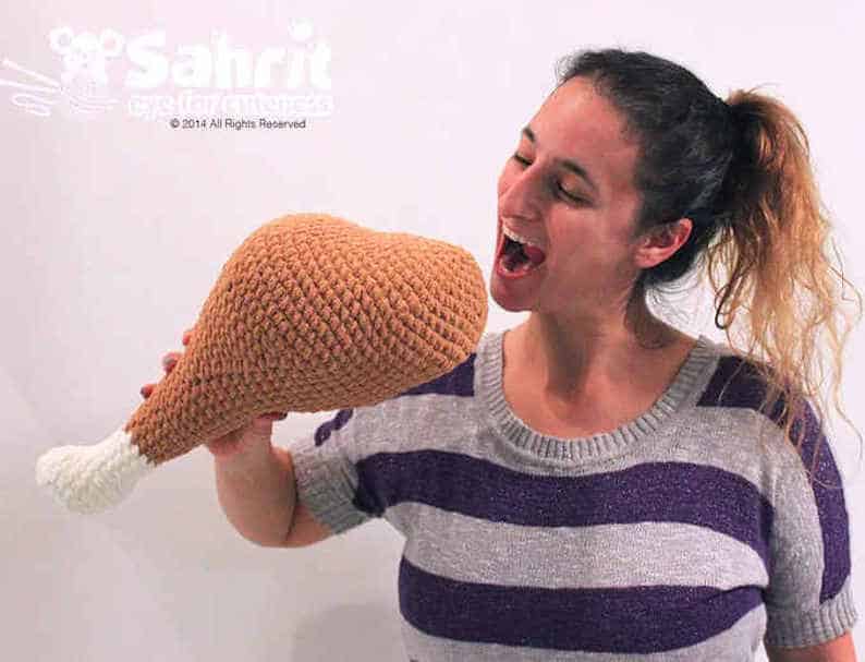 Woman pretends to eat crocheted turkey drumstick.