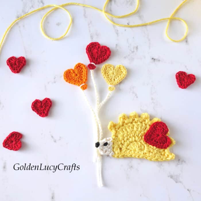 Crochet yellow hedgehog with three heart-shaped balloons applique.