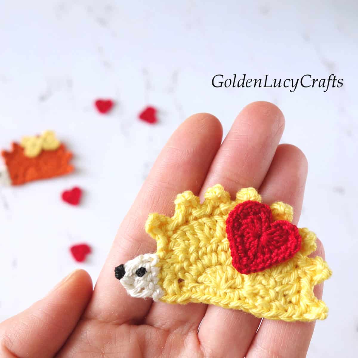 Crochet hedgehog applique in the palm of a hand.