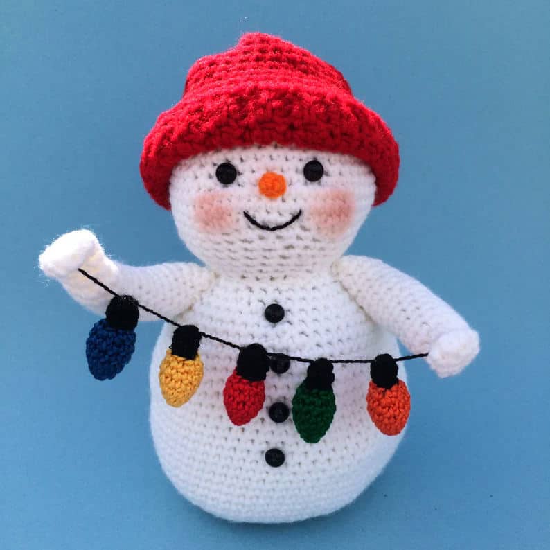 Crochet toy snowman holding christmas lights.