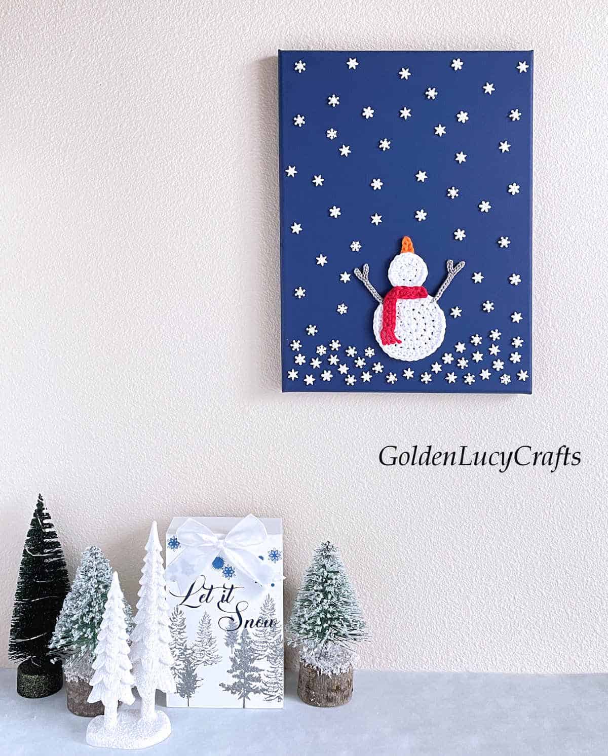 Snowman catching snowflakes crochet art hanging on the wall.
