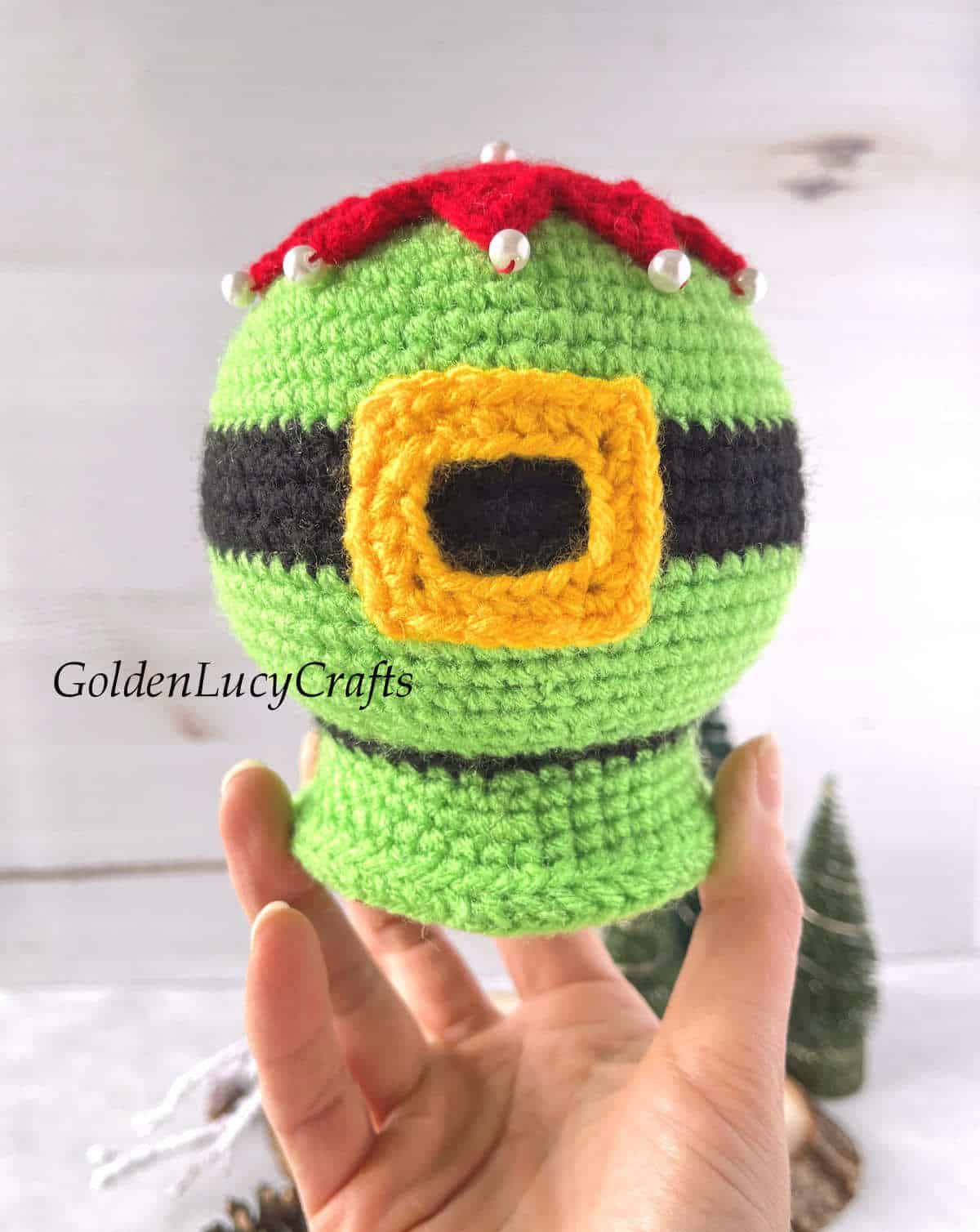 Crochet elf belly snow globe held by fingertips.