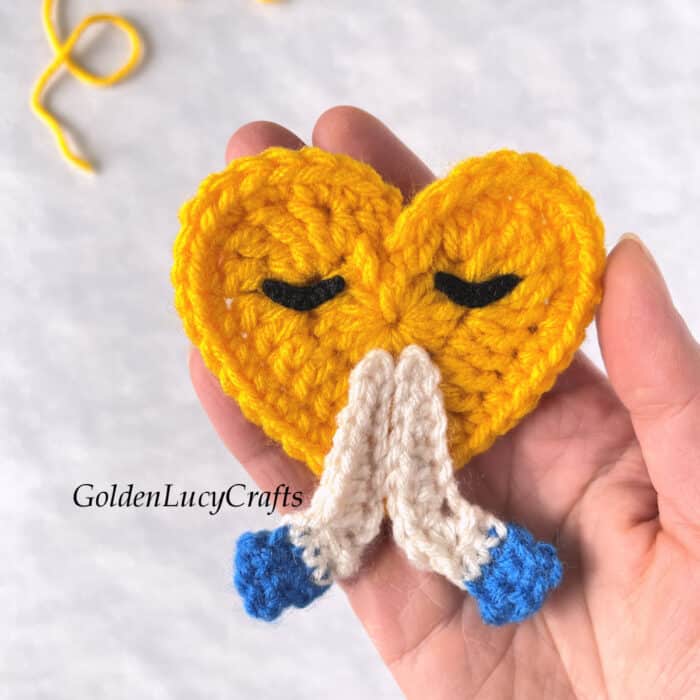 Crochet emoji applique in the palm of a hand.