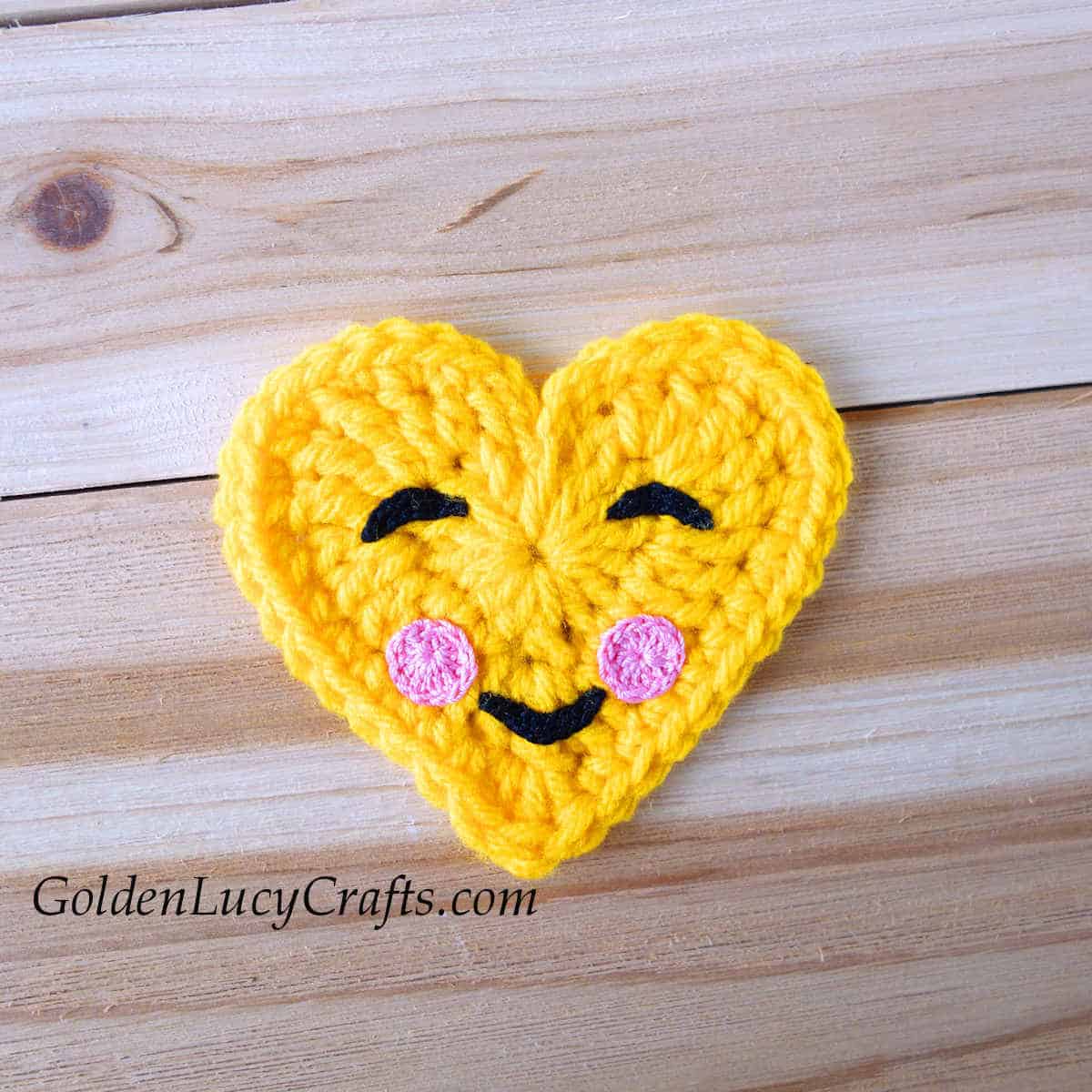 Crochet happy face emoji with heart-shaped face and pink cheeks.