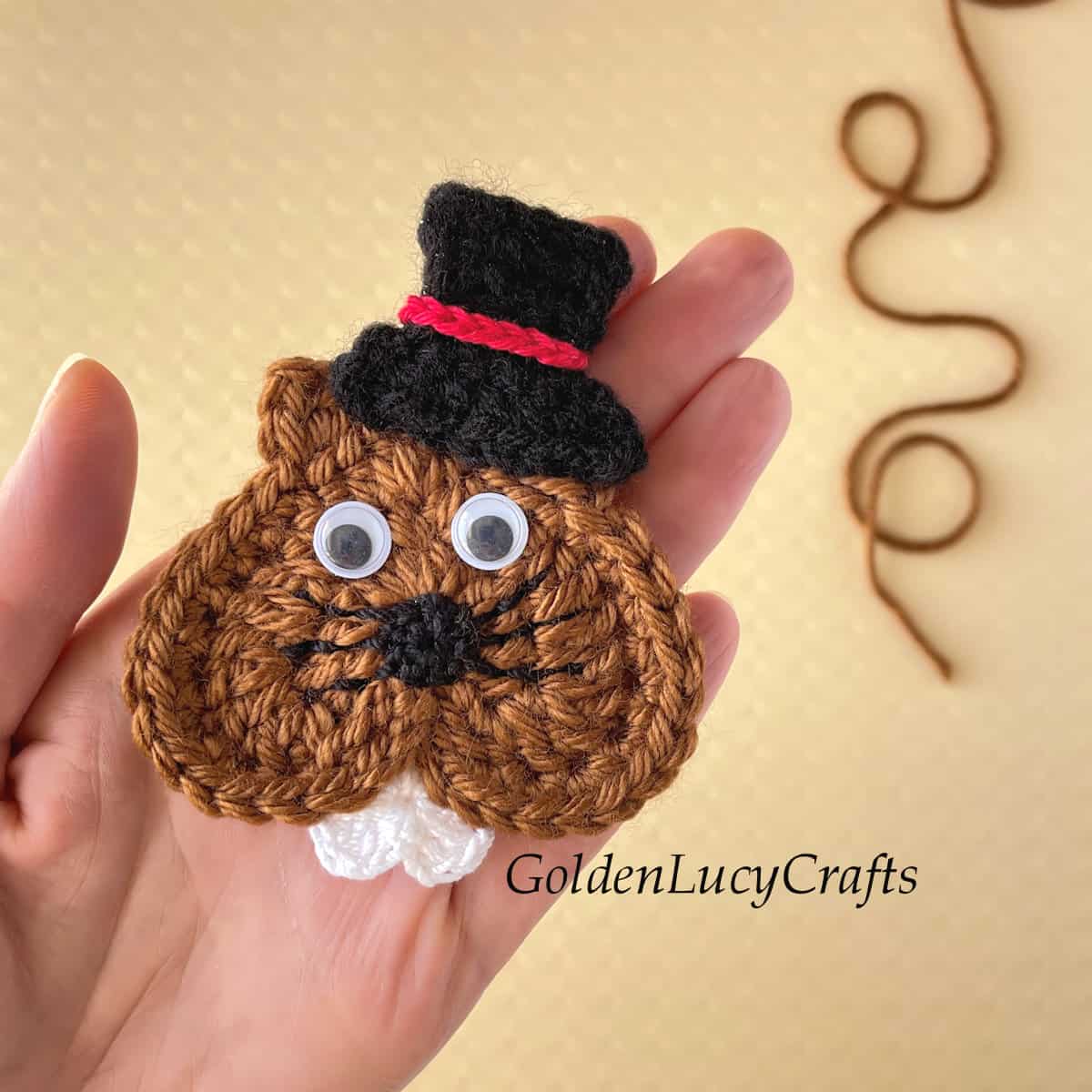 Crochet groundhog applique in the palm of a hand.