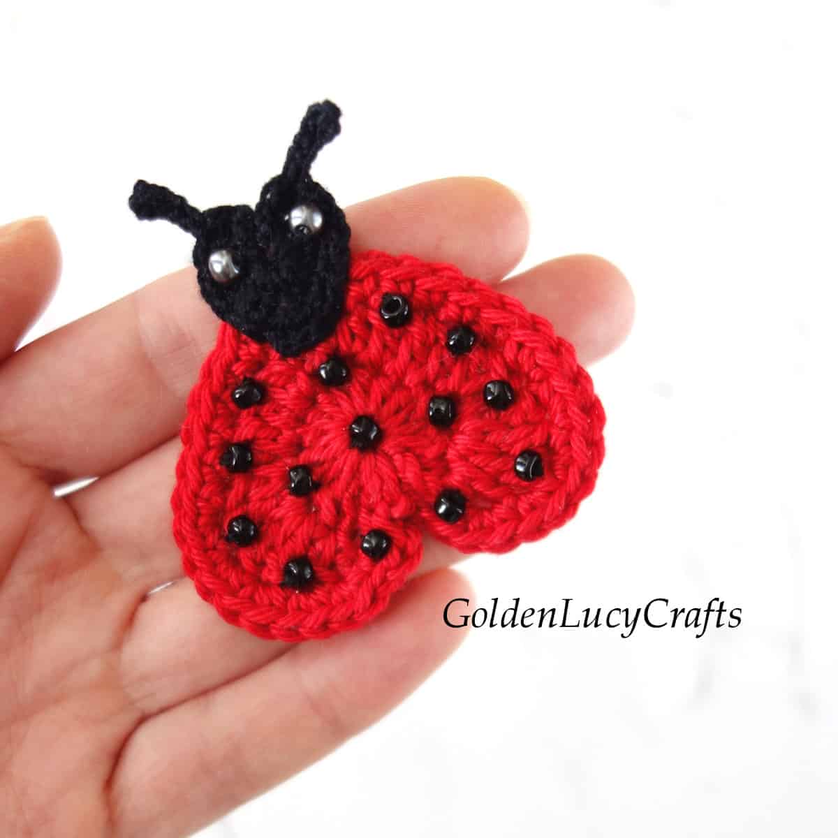 Crochet heart ladybug applique in the palm of a hand.