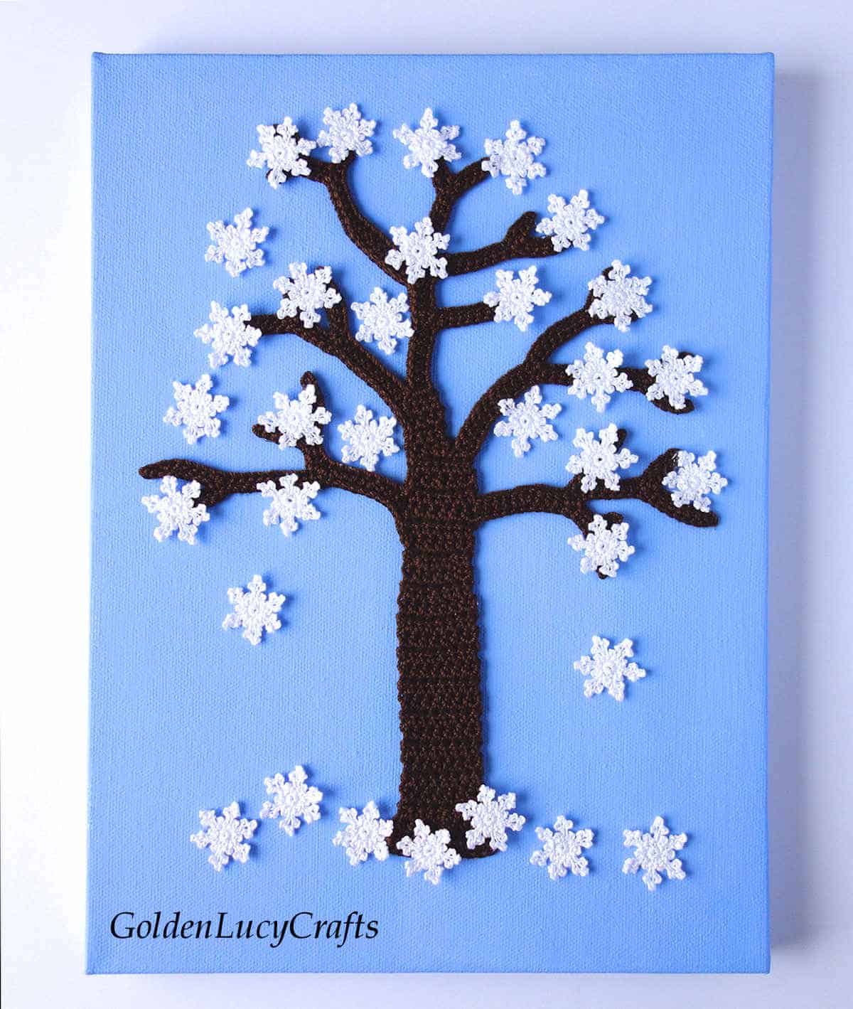 Crocheted tree and small snowflakes on the blue background, wall art.