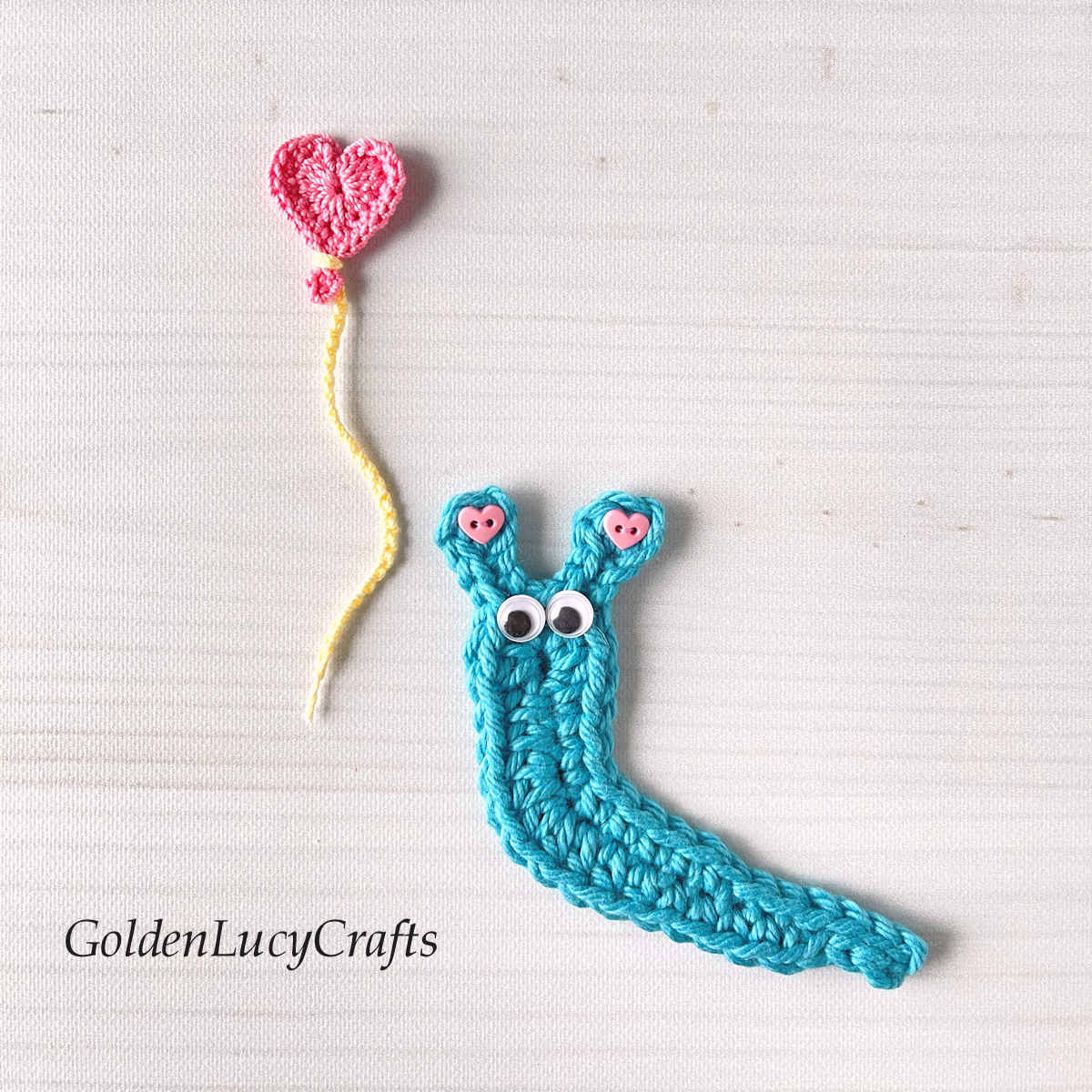 Crochet blue slug applique with pink heart balloon.