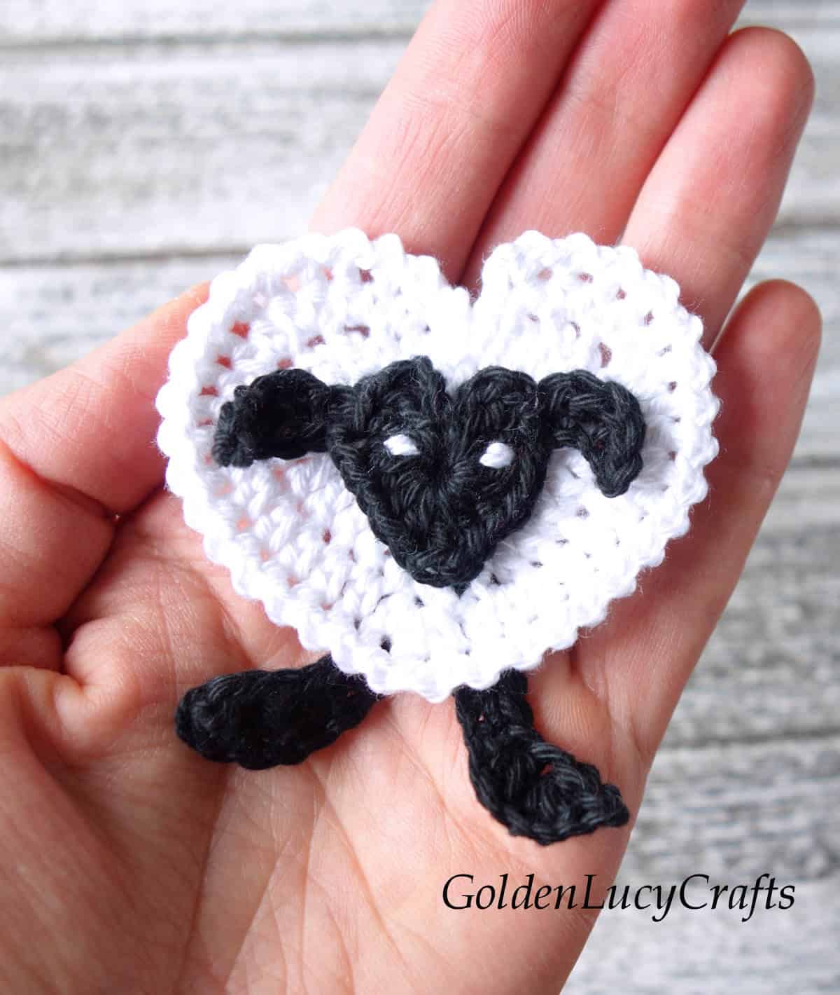 Crochet sheep applique in the palm of a hand.