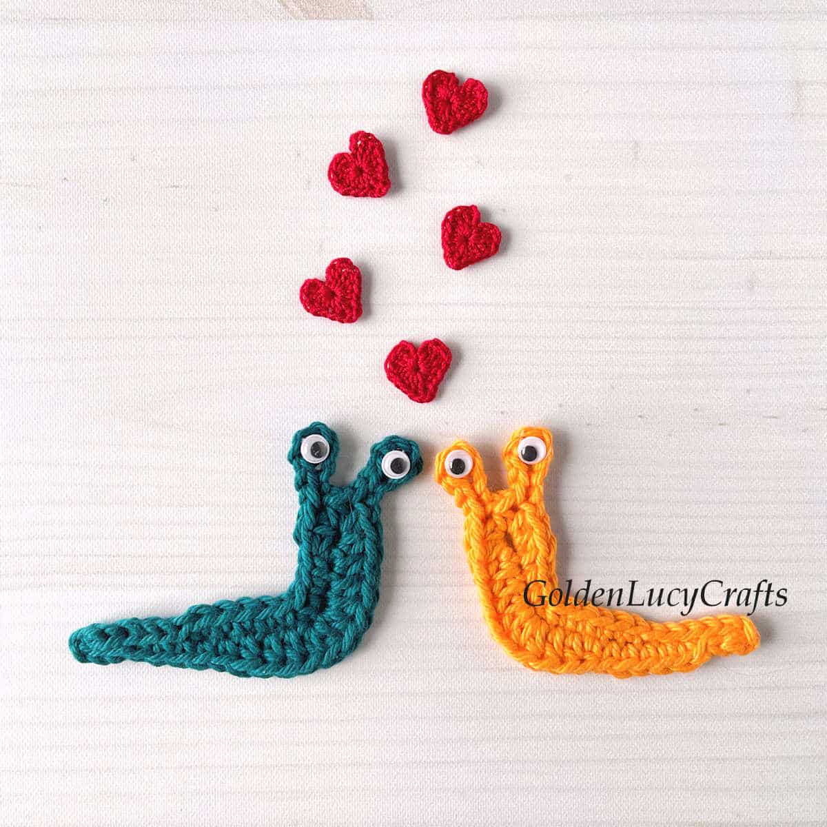 Two crochet slug appliques and small red hearts above them.
