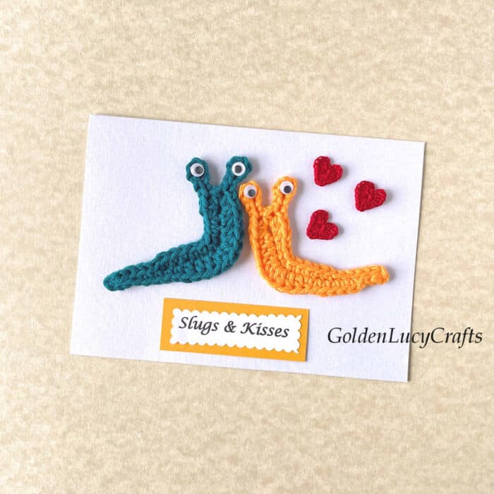 Two crocheted slugs and three crocheted small hearts on white card, note saying slugs and kisses.