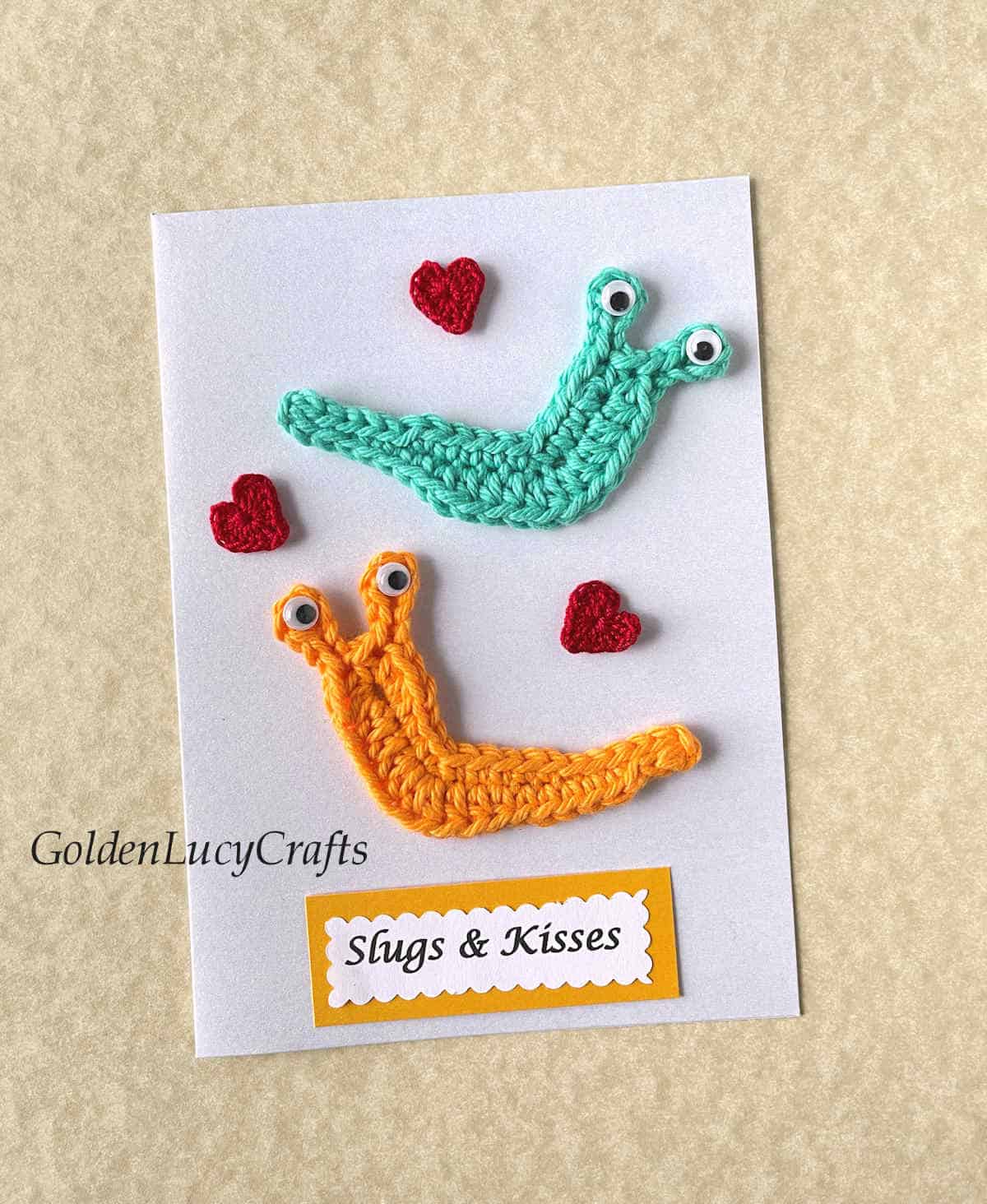 Greeting handmade card embellished with crochet slugs and hearts, note saying slugs and kisses.