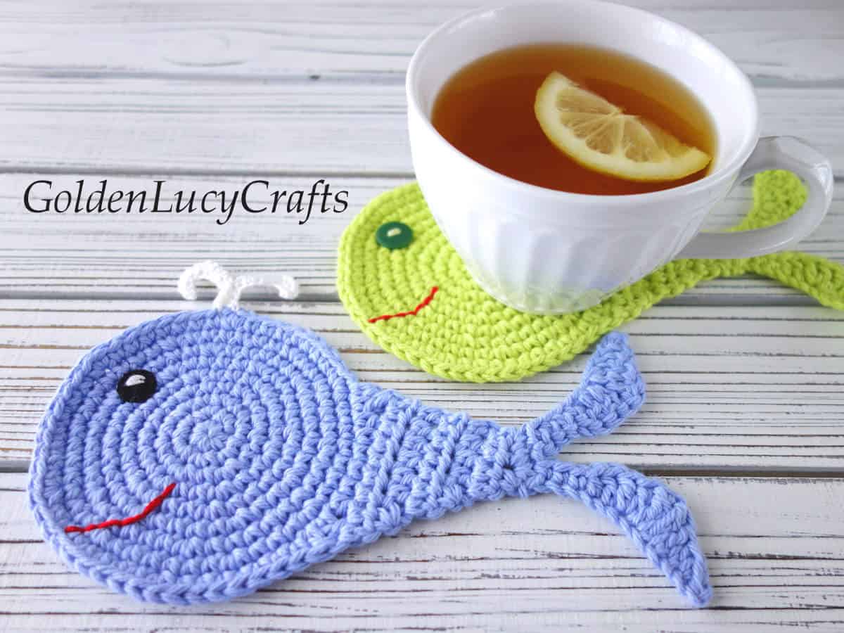 Two crocheted whale coasters, cap of a black tea with lemon.