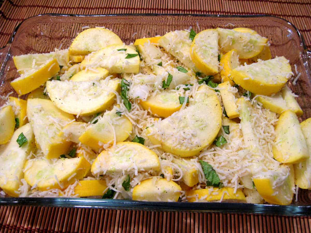Sliced yellow squash, cheese, and basil in baking dish.