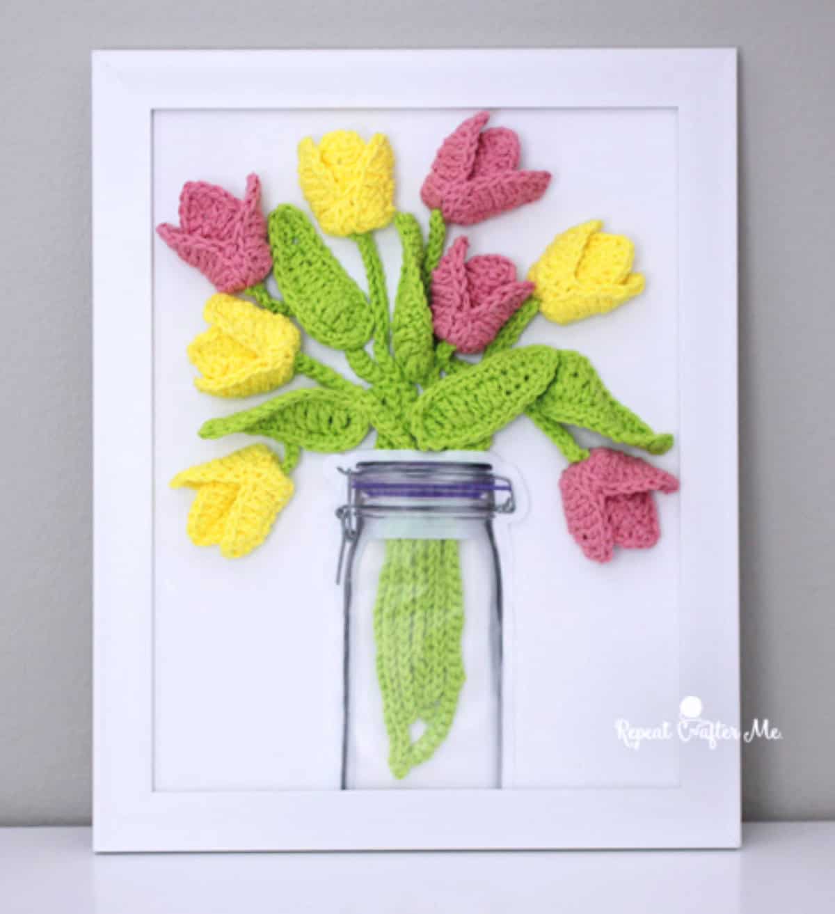 Crocheted tulips in a vase in the picture frame.