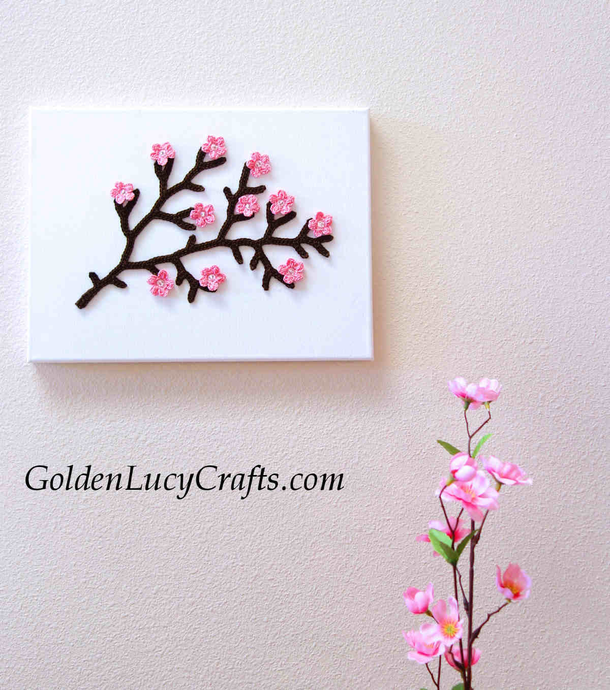 Crochet cherry tree branch on the canvas hanging on the wall.
