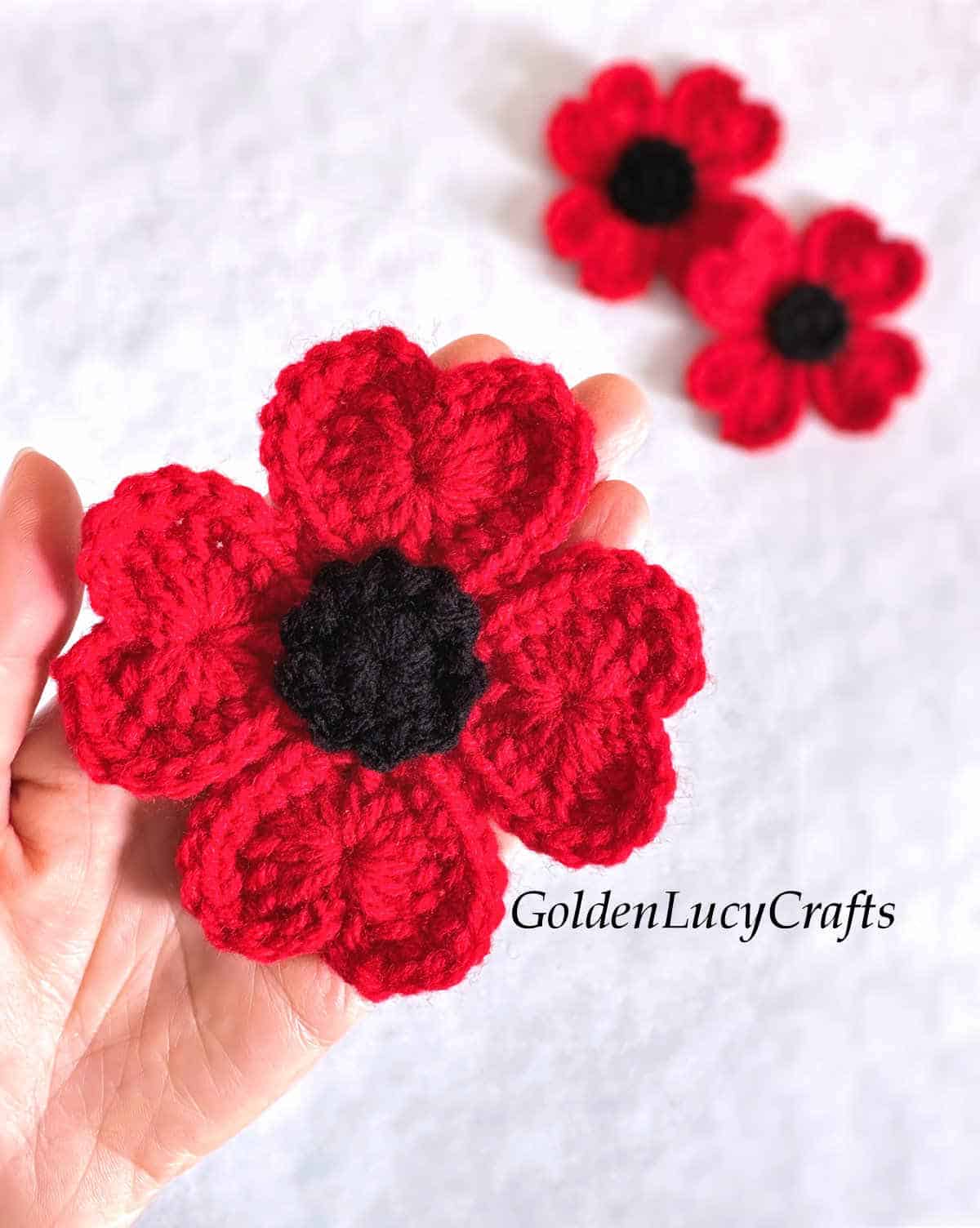 Crochet red poppy flower in the palm of a hand.
