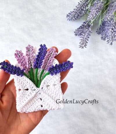 Crochet lavender envelope in the palm of a hand.