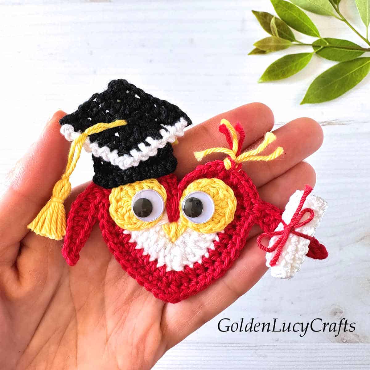 Crochet graduation owl in the palm of a hand.