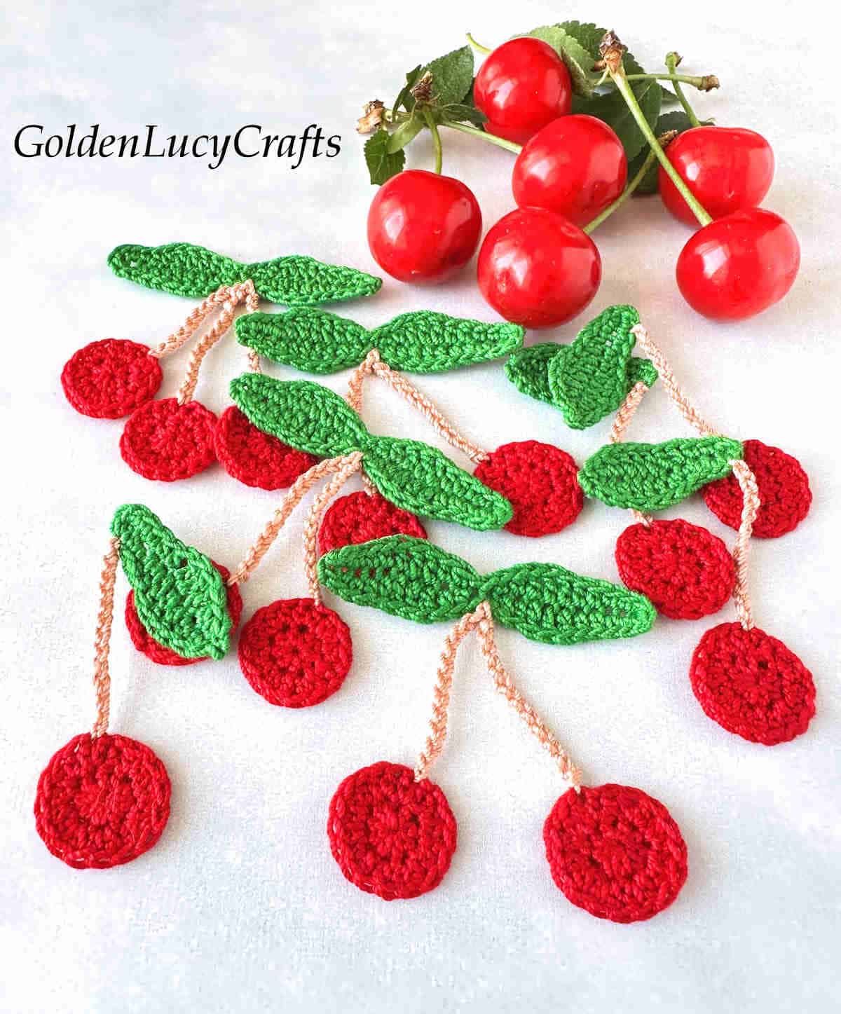 Crochet cherry appliques and real cherries in the background.